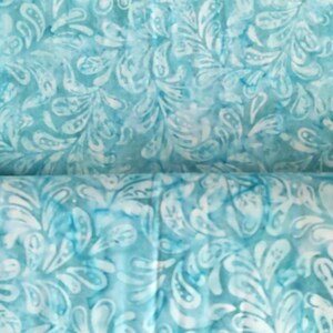 May include: Close-up of a fabric with a teal and white pattern. The design features a repeating motif of stylized leaves or feathers, creating a textured appearance. The fabric has a watercolor-like effect, with variations in color intensity.