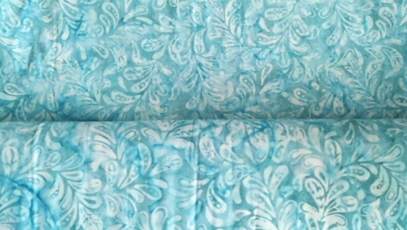 May include: Close-up of a fabric with a teal and white pattern. The design features a repeating motif of stylized leaves or feathers, creating a textured appearance. The fabric has a watercolor-like effect, with variations in color intensity.