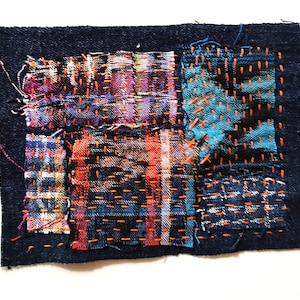 May include: A dark blue denim patch with colorful fabric squares stitched on top. The squares feature vibrant hues of red, orange, blue, and purple, with orange thread used for the stitching. The edges of the denim are frayed.