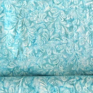May include: A roll of fabric with a repeating pattern of white, stylized leaf shapes on a light blue background. The fabric has a watercolor effect, with darker blue accents throughout.