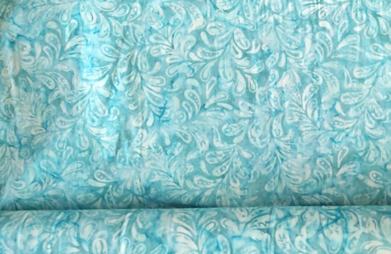 May include: A roll of fabric with a repeating pattern of white, stylized leaf shapes on a light blue background. The fabric has a watercolor effect, with darker blue accents throughout.
