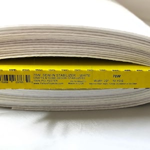 May include: A roll of white sew-in stabilizer fabric with a yellow label. The label reads "70W SEW-IN STABILIZER - WHITE" and "Width: 20" 10 YDS". The fabric is 100% polyester and is for crafts and home decor.