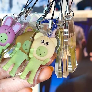 Peut inclure: Collection de breloques en acrylique transparent avec des motifs d'animaux de dessins animés, dont un ours et un lapin. Chaque breloque est attachée à une lanière noire avec un fermoir argenté. Les breloques sont de différentes nuances de vert, rose et marron.