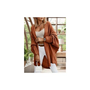 May include: A rust-colored, open-front cardigan with long sleeves. The cardigan features a relaxed fit, with a ribbed knit design on the cuffs and lower sleeves. The model is wearing a white top and white pants.
