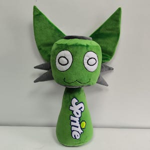 May include: A green plush toy creature with large ears and grey accents. The head features large white eyes and a smiling mouth. The body is shaped like a Sprite soda bottle, with the Sprite logo.
