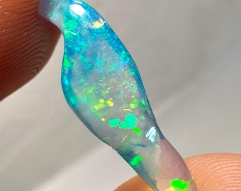 May include: A vibrant, elongated opal gemstone with a captivating play of color. The opal showcases a spectrum of blues, greens, and yellows, creating a mesmerizing display. The gemstone is held between fingers, highlighting its unique shape and iridescent qualities.