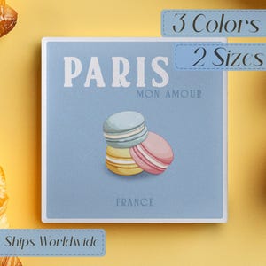 May include: A square, pale blue graphic featuring the word "PARIS" in white, with "MON AMOUR" beneath. Three macarons in pastel shades are stacked below the text. The word "FRANCE" is at the bottom of the graphic.