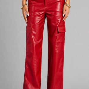 Op de afbeelding: Felrode cargo broek van imitatieleer. Deze broek met wijde pijpen heeft twee cargozakken op de benen, een knoop- en ritssluiting en riemlussen. De broek is effen van kleur en heeft een lichte glans.