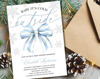 May include: A baby shower invitation with the text "Baby It's Cold Outside" in a script font. The invitation features a watercolor bow in shades of blue and white, surrounded by snowflakes. An envelope and pinecones are in the background.