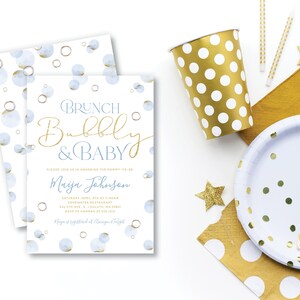 Peut inclure: Une invitation à une baby shower avec le texte "Brunch, Bubbly & Baby" en or et bleu, ainsi que des fournitures de fête assorties. L'image comprend une tasse à pois dorés, une assiette, des pailles et des décorations en forme d'étoile.