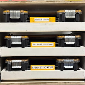 May include: Three drawers in a wooden cabinet with yellow labels. The top drawer is labeled "HEX HEAD SCREWS", the middle drawer is labeled "PHILLIPS AND SQUARE HEAD", and the bottom drawer is labeled "CABINET SCREWS".