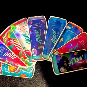 May include: An assortment of Alani Nu Energy drink cans, featuring various flavors like Hawaiian Shaved Ice, Watermelon Wave, and Cosmic Stardust. The cans are brightly colored with fruit and space-themed graphics, and the text "Alani Nu Energy" is prominently displayed.