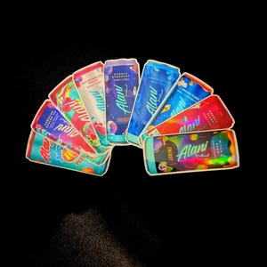 May include: A collection of Alani Nu energy drink cans in various flavors, including Cosmic Stardust, Watermelon Wave, and Hawaiian Shaved Ice. Each can features colorful designs and the Alani Nu logo, with the word "Energy" prominently displayed.