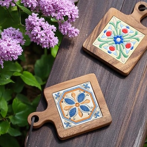 May include: Two wooden cutting boards with decorative ceramic tile inserts. The tiles feature floral patterns in blue, orange, red, and green. The boards have a handle with a hole for hanging.