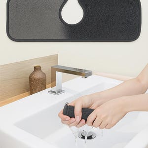 May include: A dark gray and light gray absorbent and washable sink mat with a U-shaped cutout. The text "Super Absorbent & Washable" is at the top. A person is wringing out a dark gray absorbent pad over a white sink.