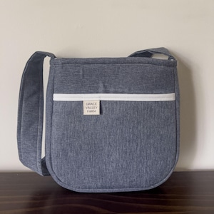 May include: A gray crossbody bag with a white stripe and a brown leather patch that says "GRACE VALLEY FARM".