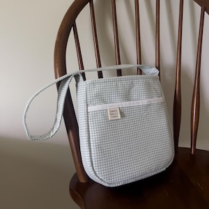 May include: A light blue and white gingham crossbody bag with a white strap and a small white label that says "Grace Valley Farms".