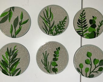 Puede incluir: Seis posavasos redondos con una superficie texturizada de color gris claro y un borde gris oscuro. Cada posavasos presenta un diseño botánico verde diferente, que incluye hojas y helechos.