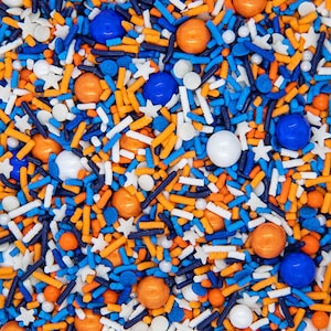 May include: A close-up of a variety of colorful sprinkles, including blue, orange, and white. The sprinkles are in the shape of stars, balls, and long, thin sticks.