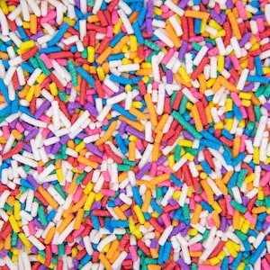 May include: A close-up image of colorful sprinkles. The sprinkles are long and thin, and they are arranged in a random pattern. The colors of the sprinkles include red, orange, yellow, green, blue, purple, and white.