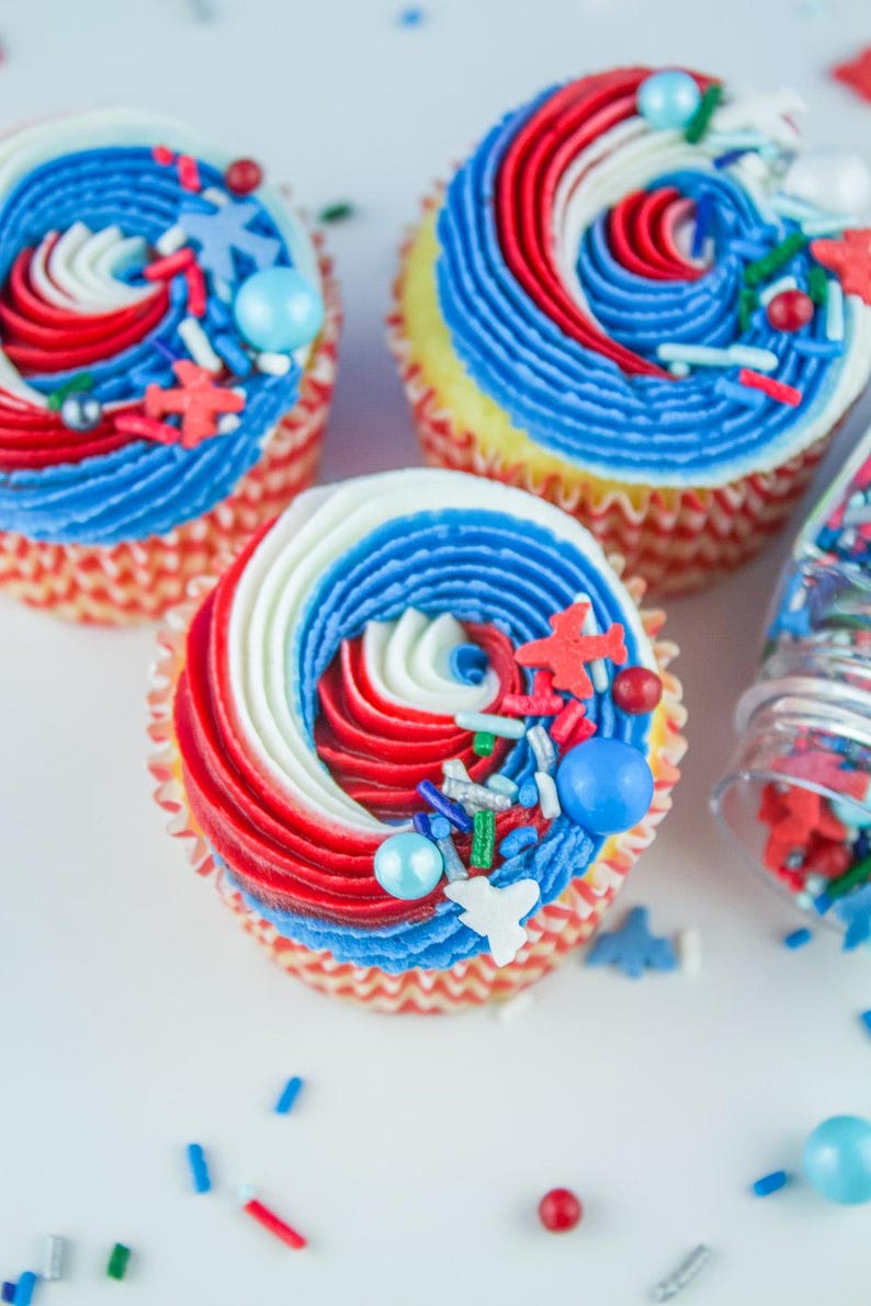 May include: Three red, white, and blue cupcakes with sprinkles and candy. The cupcakes are decorated with a swirl of frosting and are topped with red, white, and blue sprinkles and candy.