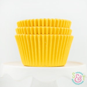 May include: A stack of yellow cupcake liners. The liners are made of paper and have a fluted design.