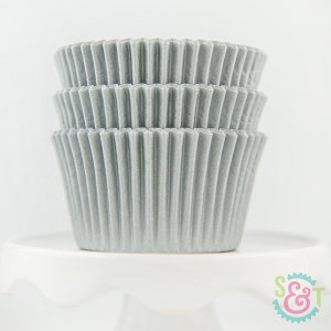 May include: A stack of silver cupcake liners. The liners are made of paper and have a fluted design.
