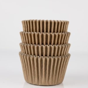 May include: A stack of four brown, corrugated paper cupcake liners. The liners are nested inside each other, with a fluted edge design. The image is set against a white background.