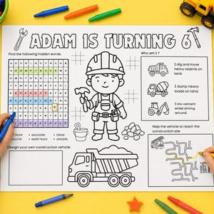 May include: A white activity placemat with black line art featuring the text ADAM IS TURNING 6, a construction worker character, a word search puzzle, a maze, and construction vehicle illustrations, surrounded by colourful crayons and toy trucks.
