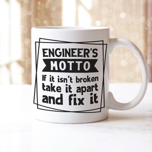 May include: White ceramic mug featuring the text "ENGINEER'S MOTTO" in a black frame. The motto reads "If it isn't broken take it apart and fix it" in black text. The mug has a curved handle.