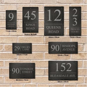 May include: A collection of black slate house number signs with white lettering. The signs feature various house numbers and street names, including "9 Montrose Avenue", "45 Kings Road", "12 Queens Road", "23 Princes Court", "29 Drury Lane", "90 Bishops Avenue", "90 Conduit Street", and "152 Bleasdale Ave.". The signs are displayed on a brick wall and are available in various sizes.