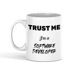 May include: White ceramic mug with a curved handle. The mug features the text "TRUST ME" in bold black letters above the phrase "I'm a SOFTWARE DEVELOPER" in a handwritten style font.