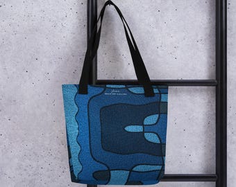 Puede incluir: Un bolso tote azul con un diseño geométrico en tonos azules. El bolso tiene asas negras y el texto "flime BOLD ART GALLERY" está impreso en la parte delantera. El bolso está colgado de un estante de metal negro.