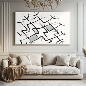 Pode incluir: Impressão de arte abstrata com um design geométrico de linhas pretas, detalhes em rosa pálido e dois quadrados verde claro sobre um fundo branco. A obra de arte é emoldurada em uma moldura dourada e pendurada acima de um sofá bege.