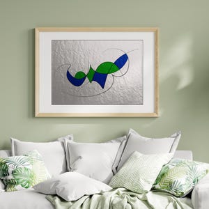 Pode incluir: Impressão de arte abstrata em uma moldura de madeira clara. A obra de arte apresenta um fundo prateado com formas geométricas azuis e verdes e linhas curvas pretas. A arte emoldurada é exibida acima de um sofá branco com almofadas decorativas.