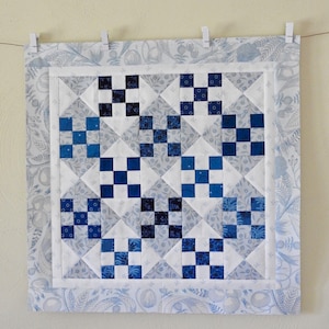 May include: A blue and white quilt with a geometric pattern. The quilt is made of squares and triangles, and it is bordered with a floral print.