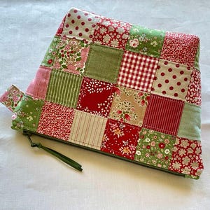 May include: A patchwork zippered pouch featuring a variety of fabrics in red, green, pink, and cream. The fabrics include floral, polka dot, striped, and gingham patterns. The pouch has a green zipper and pull.