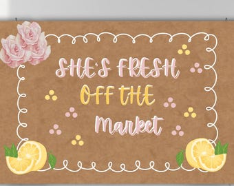 May include: A rectangular sign with the text "She's Fresh Off The Market" in a whimsical font. The sign is brown with a white border, pink roses, and lemon illustrations. The text is in pink and yellow.