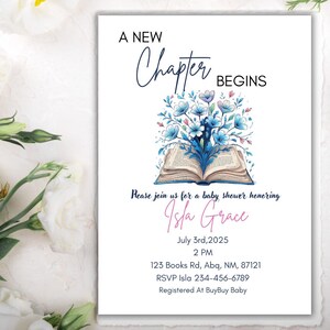 May include: Baby shower invitation with the text "A New Chapter Begins" and "Isla Grace". The invitation features an open book with blue floral arrangements. White flowers surround the invitation.