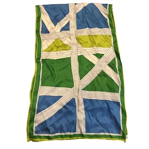 May include: A rectangular scarf featuring a geometric pattern of blue, lime green, and dark green blocks intersected by white bands with thin black pinstripes. The scarf has a lime green border and the signature "Vera" printed in the bottom corner.