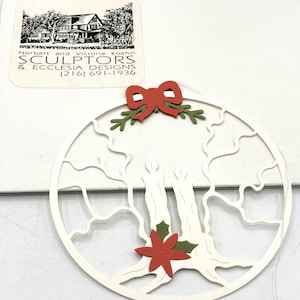 Könnte beinhalten: Weißer Papier-Weihnachtsschmuck mit einem Baumdesign. Der Schmuck hat eine rote Schleife und einen Weihnachtsstern. Hergestellt von Sculptors & Ecclesia Designs.