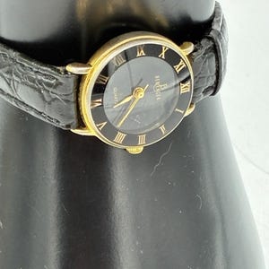 May include: A Berenger quartz wristwatch featuring a round gold-tone case, a black dial with gold-tone Roman numeral hour markers, and a black textured leather strap. The watch face displays the brand name Berenger and the word Quartz.