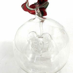 Könnte beinhalten: Transparenter Weihnachtsbaumschmuck aus Glas mit einem herzförmigen Design im Inneren. Aufgehängt an einem rot-grün-goldenen Band. Der kugelförmige Schmuck ist transparent und zeigt das Herz. Eine festliche Dekoration.
