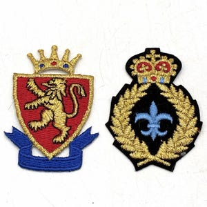 May include: Two embroidered patches. The left patch features a gold lion on a red shield topped with a gold crown and a blue ribbon at the base. The right patch displays a light blue fleur-de-lis inside a gold wreath, topped with a crown.
