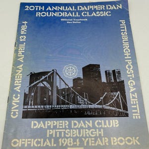 May include: A blue 1984 Dapper Dan Roundball Classic official yearbook featuring a black and white illustration of a bridge and city skyline. The cover includes the text 20th Annual Dapper Dan Roundball Classic, Civic Arena April 13 1984, and Pittsburgh Post-Gazette.