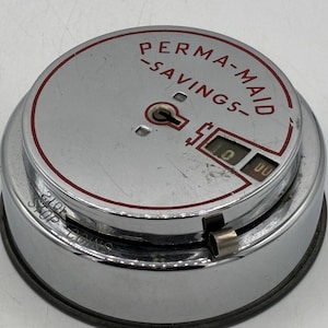 May include: A vintage Perma-Maid savings bank with a chrome finish. The top of the bank features the words "PERMA-MAID -SAVINGS-" in red lettering. The bank has a coin slot and a display showing "00". The words "STOP COINS" are visible.