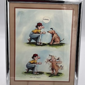 May include: Framed cartoon print with a silver metal frame. The print depicts a person and a dog in two panels. The top panel shows the person saying "SHAKE" to the dog. The bottom panel shows the dog shaking. The artist's name is "GARY PATTERSON".