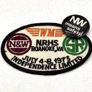 Könnte beinhalten: Ein ovaler gestickter Aufnäher mit weißem Hintergrund und schwarzem Rand. Er zeigt den Text N&W, NRHS ROANOKE, VA, SR und JULY 4-8, 1973 INDEPENDENCE LIMITED. Ein runder schwarzer Anstecker mit dem weißen Text NW means safety ist befestigt.