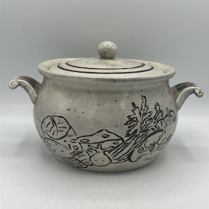 Puede incluir: Una sopera de cerámica moteada de color blanquecino con tapa y asas. La sopera presenta una ilustración dibujada a mano de setas y verduras. La tapa tiene un pequeño pomo redondo. Las asas tienen un diseño rizado.