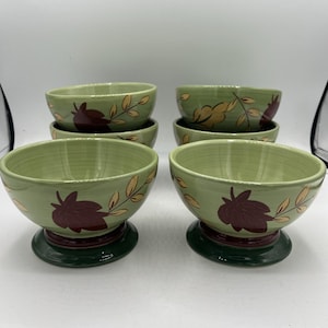 Pode incluir: Conjunto de seis tigelas de cerâmica verde com um desenho de folhas. As tigelas têm uma base verde escura e um padrão de folhas castanhas com detalhes dourados. Ideais para servir sopa, cereais ou outros pratos.
